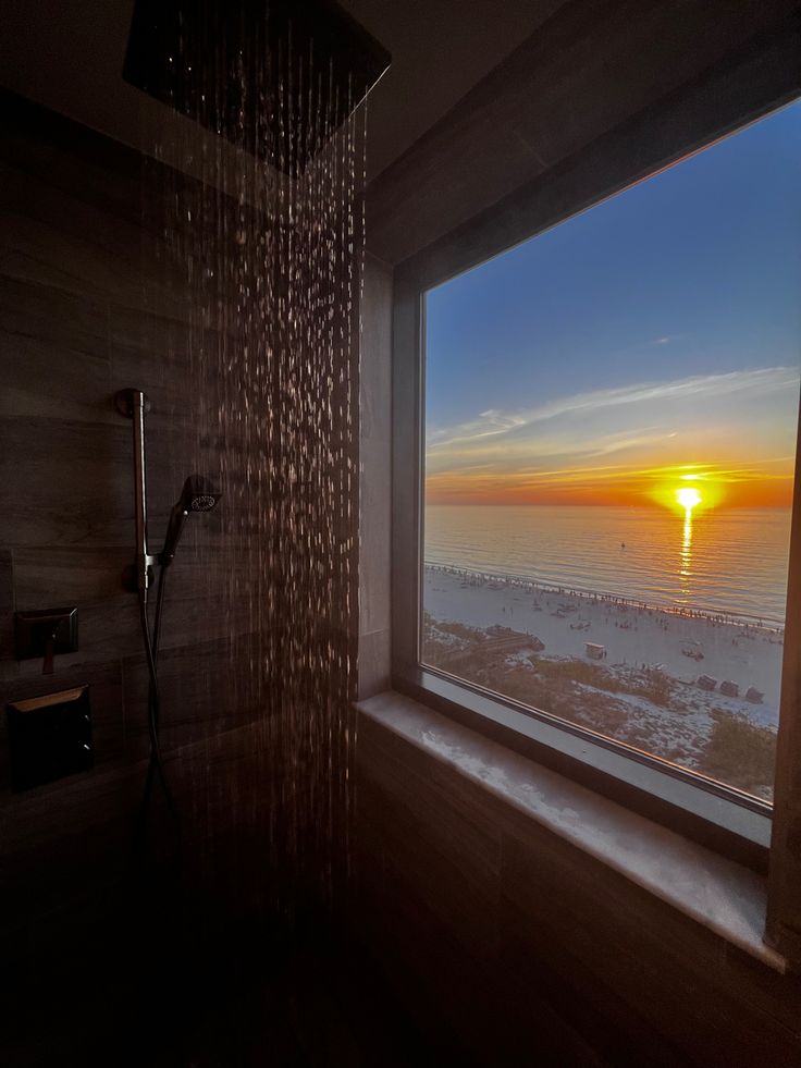 the sun is setting over the ocean from a window in a bathroom with a shower head