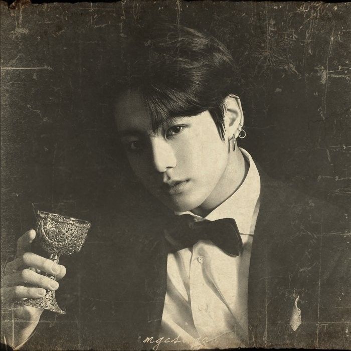 a young man in a tuxedo holding a glass and looking at the camera