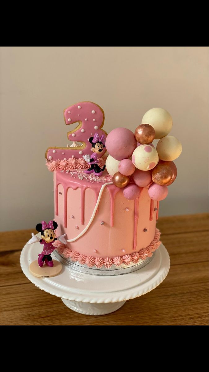 a pink cake with minnie mouse decorations on top and balloons in the shape of numbers