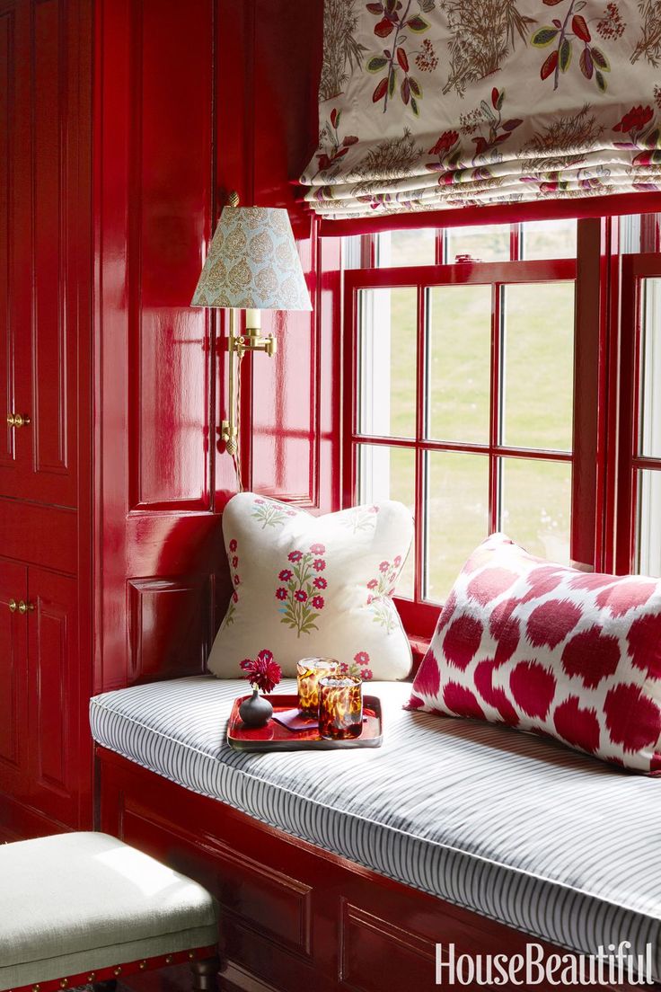 a bedroom with red painted walls and white bedding, along with a bench in front of the window