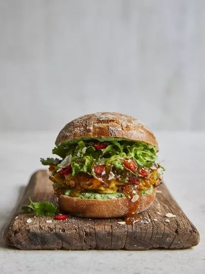 a sandwich with lettuce, tomato and other toppings on a wooden cutting board