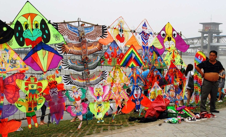 a man standing next to a wall covered in lots of kites and other items