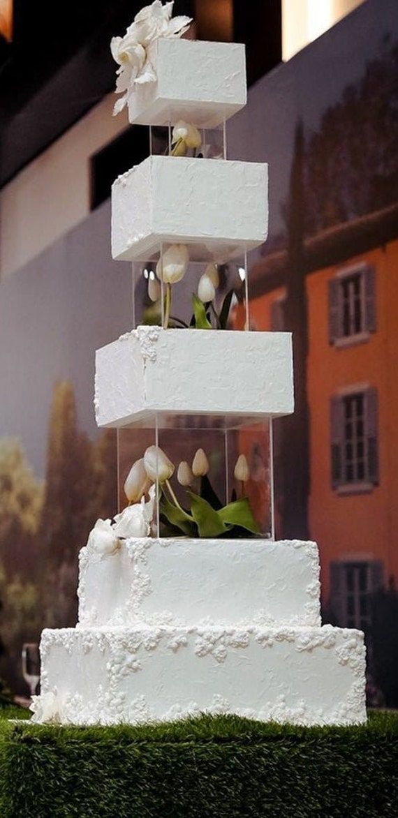 a tall white cake sitting on top of a lush green field next to a building