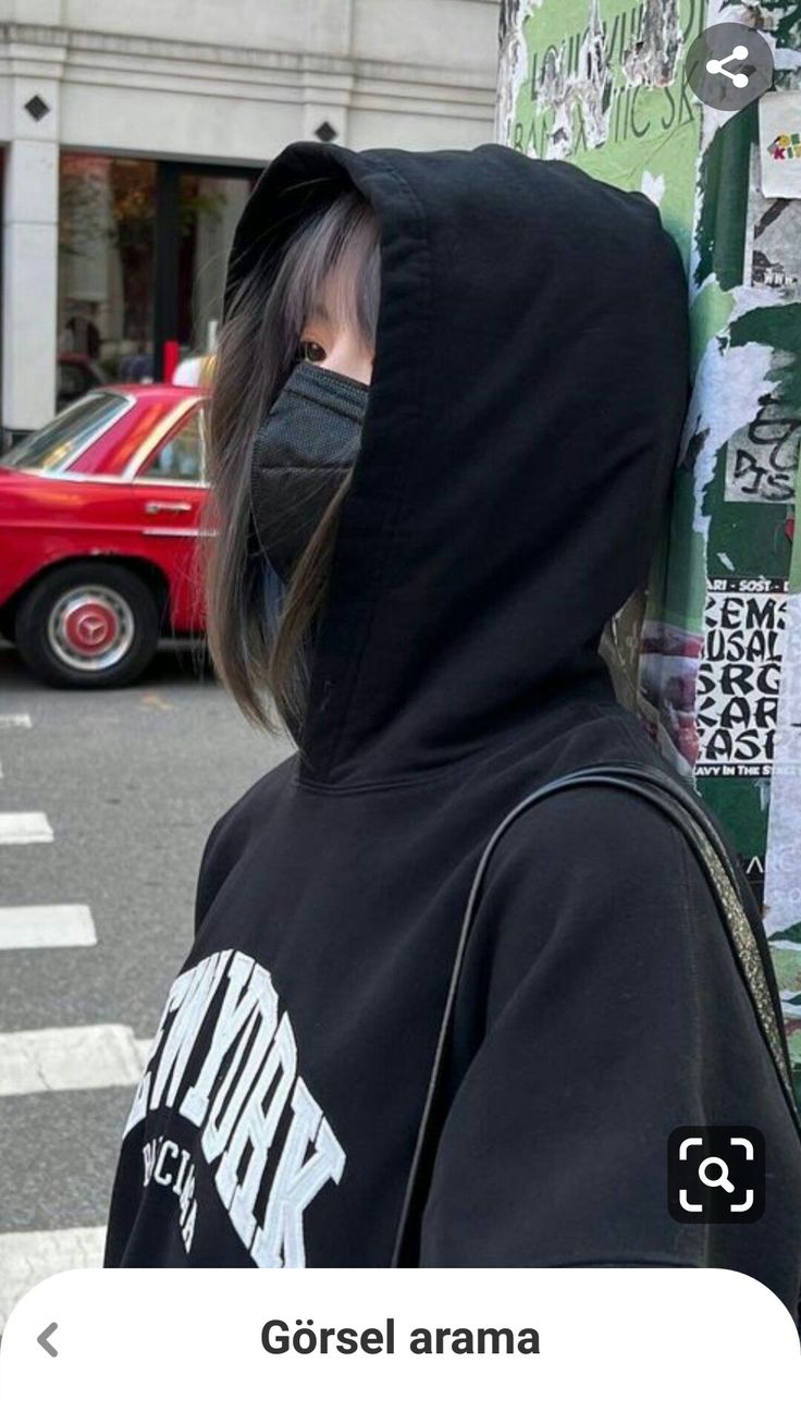 a person wearing a face mask standing in front of a pole with graffiti on it