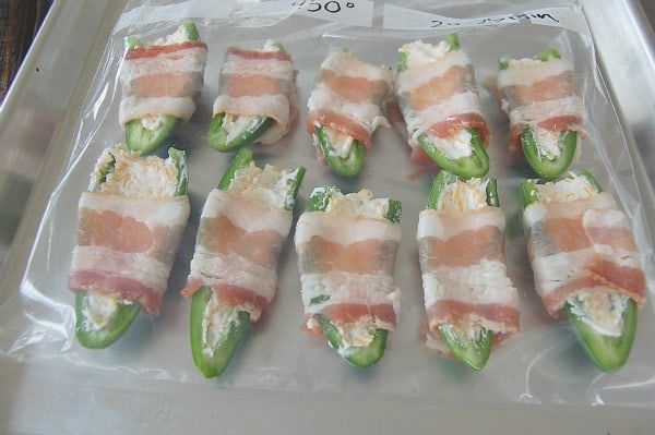 several green peppers wrapped in bacon and cheese on a plastic tray, ready to be cooked