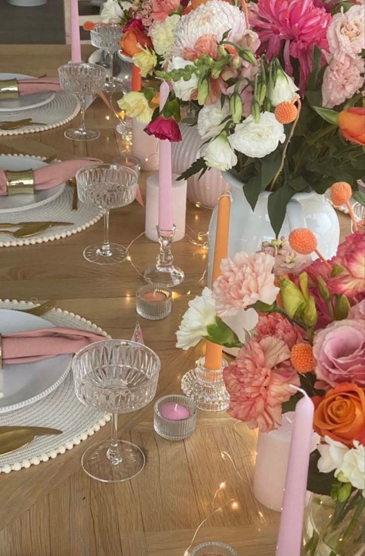 the table is set with pink and white flowers in vases, candles, and plates