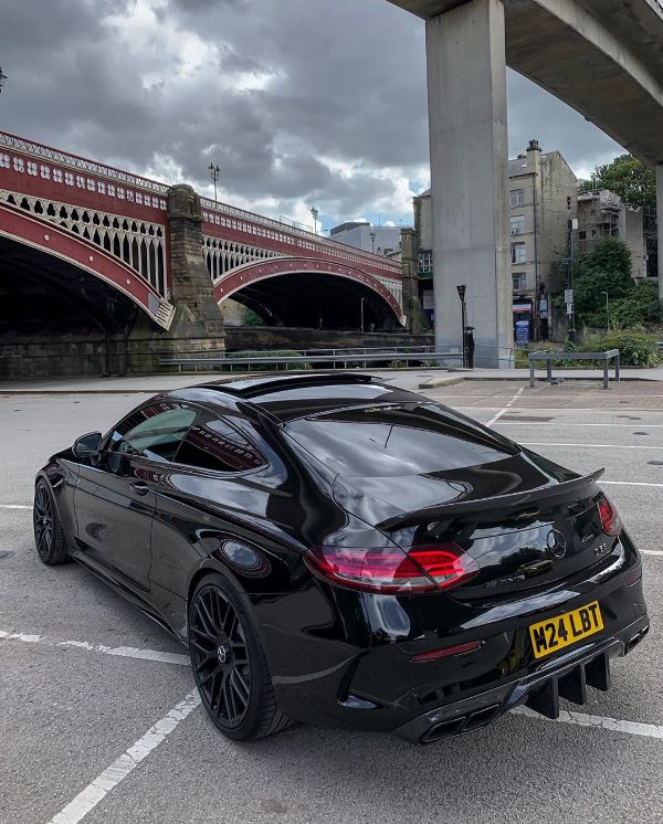 a black sports car parked in a parking lot next to a bridge and some buildings