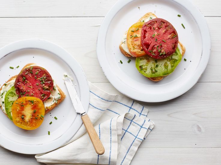 two white plates with tomatoes and cheese on them next to a knife, fork and napkin