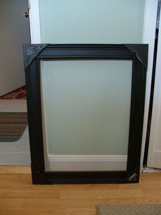 a black frame sitting on top of a hard wood floor next to a white door