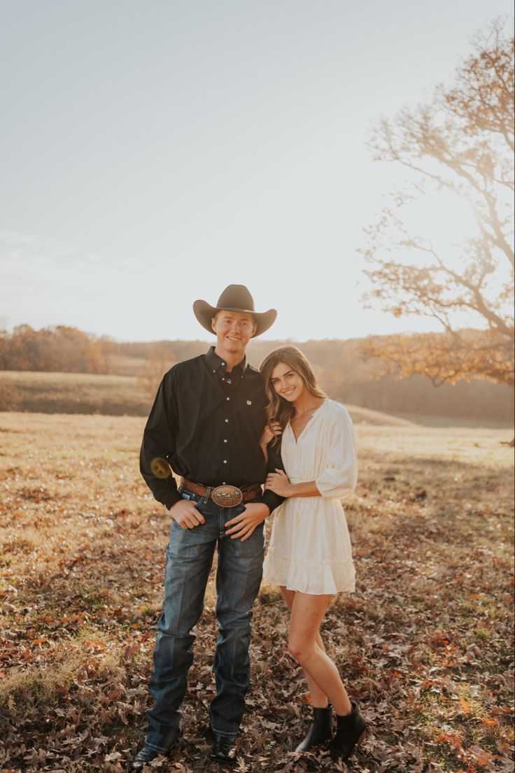 a man and woman standing next to each other in a field with leaves on the ground