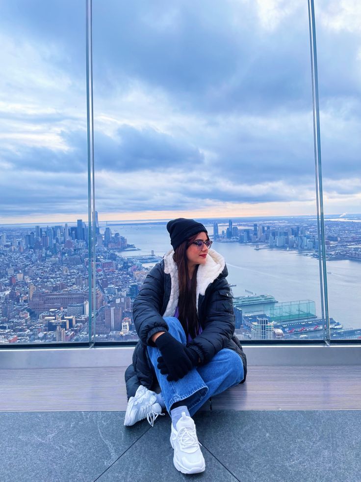 a woman sitting on top of a tall building next to a cityscape in the distance