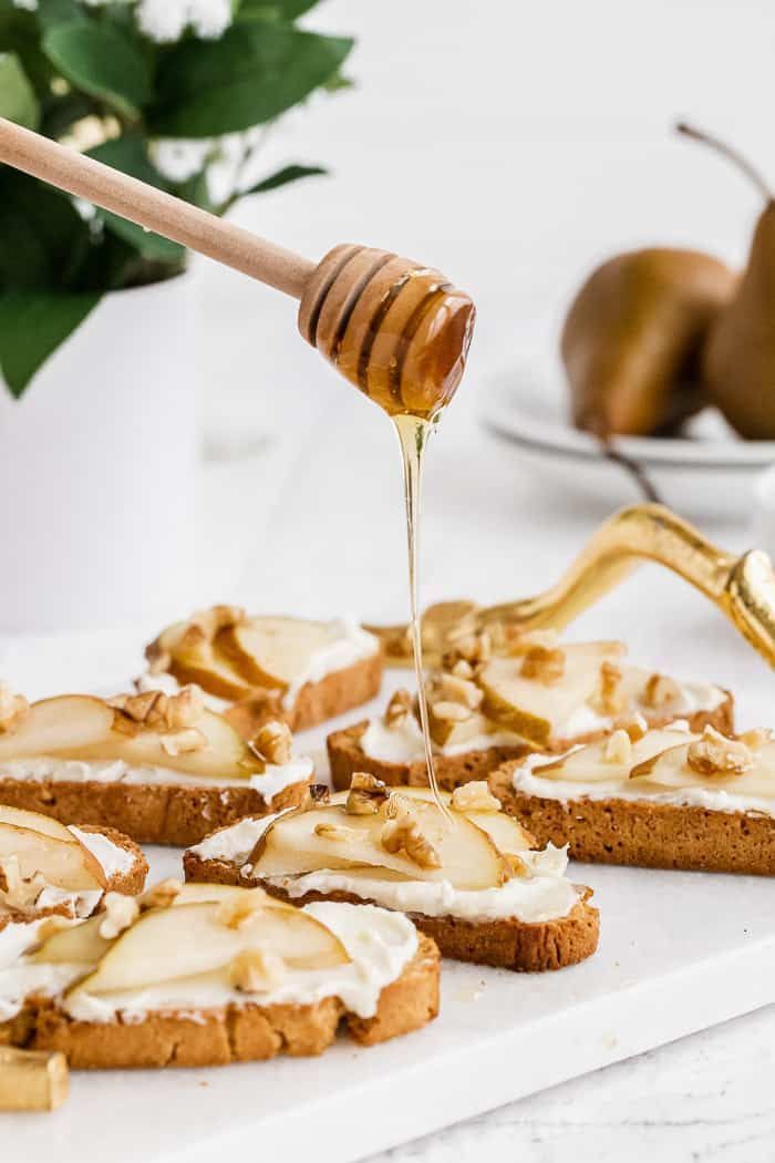 a person drizzling honey onto some cookies on a table with pears in the background