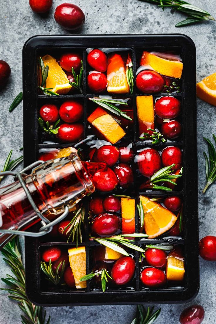 a glass bottle filled with liquid surrounded by cranberries, oranges and rosemary