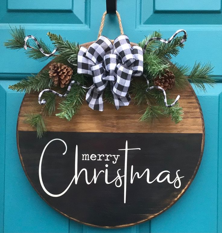 a merry christmas sign hanging on a blue door with pine cones and evergreens around it