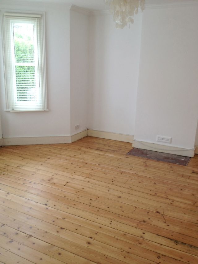 an empty room with hard wood floors and a window in the corner on the far wall