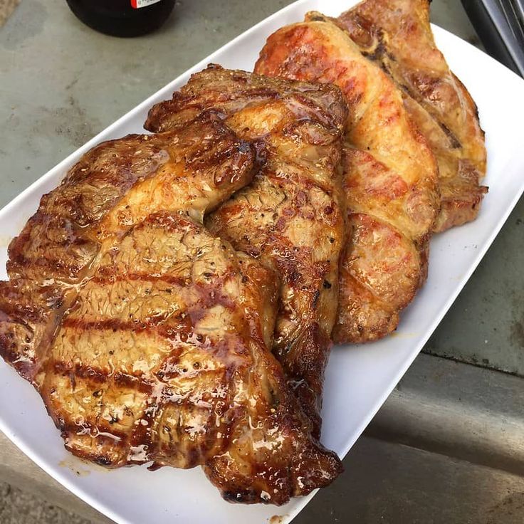 some meat on a white plate next to a bottle of beer and a can of soda