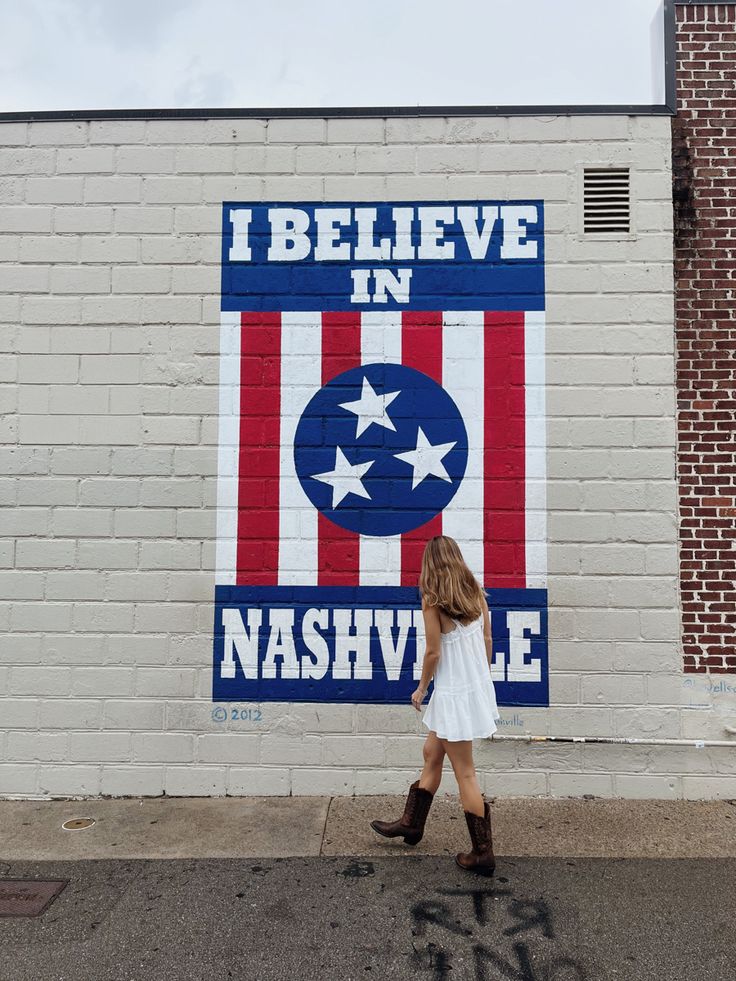 a woman walking past a wall painted with an american flag and the words i believe in nashville