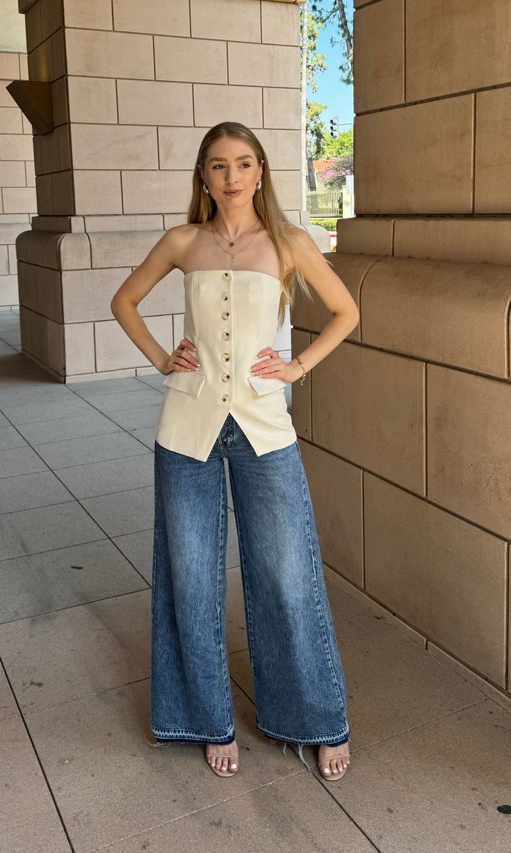 a woman standing in front of a brick wall wearing wide jeans and a white top