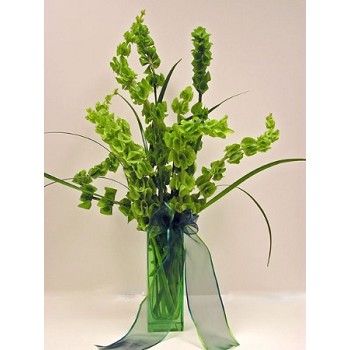 a green vase filled with lots of flowers on top of a white tablecloth covered floor