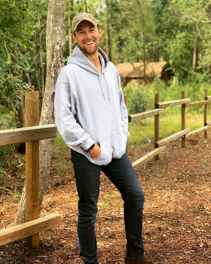 a man standing in front of a tree wearing a hat and smiling at the camera