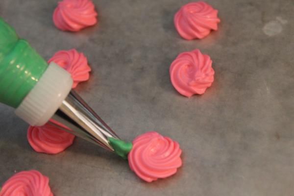 a person is using a green plastic tool to decorate cupcakes with pink frosting