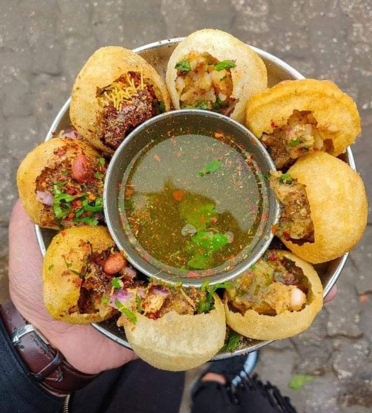 a person holding a metal bowl filled with different types of food on top of it