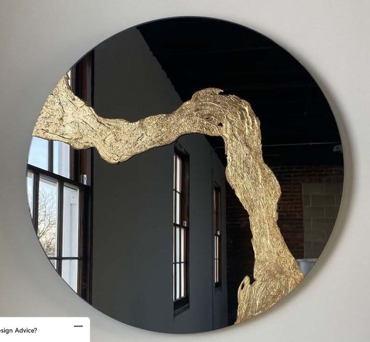 a round mirror with a tree branch in the middle on a wall next to a window