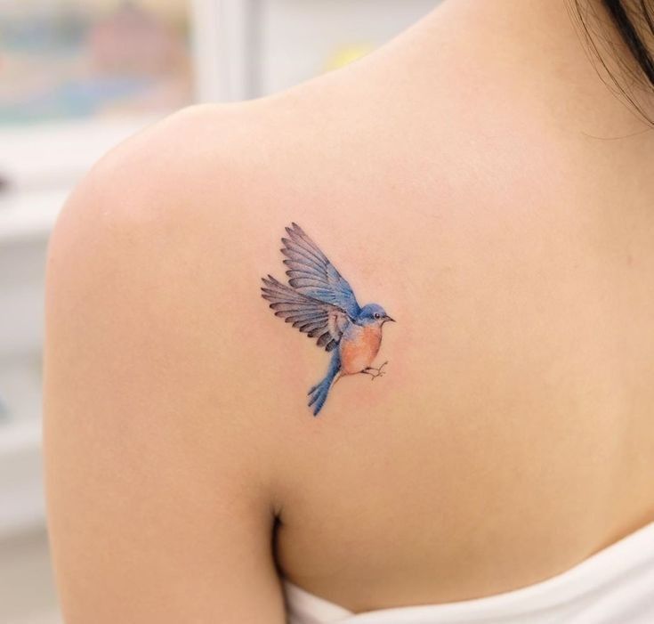 a small blue bird tattoo on the back of a woman's upper arm and shoulder