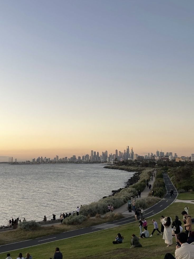 many people are sitting on the grass by the water