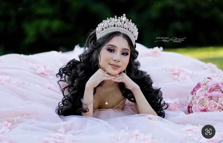 a beautiful young lady wearing a tiara laying on the ground with flowers in front of her