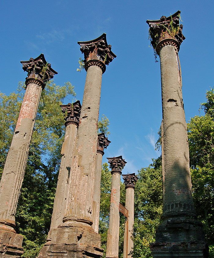 four tall stone pillars in the middle of a park with trees and blue sky behind them