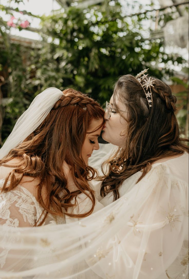 two women in wedding dresses are kissing each other