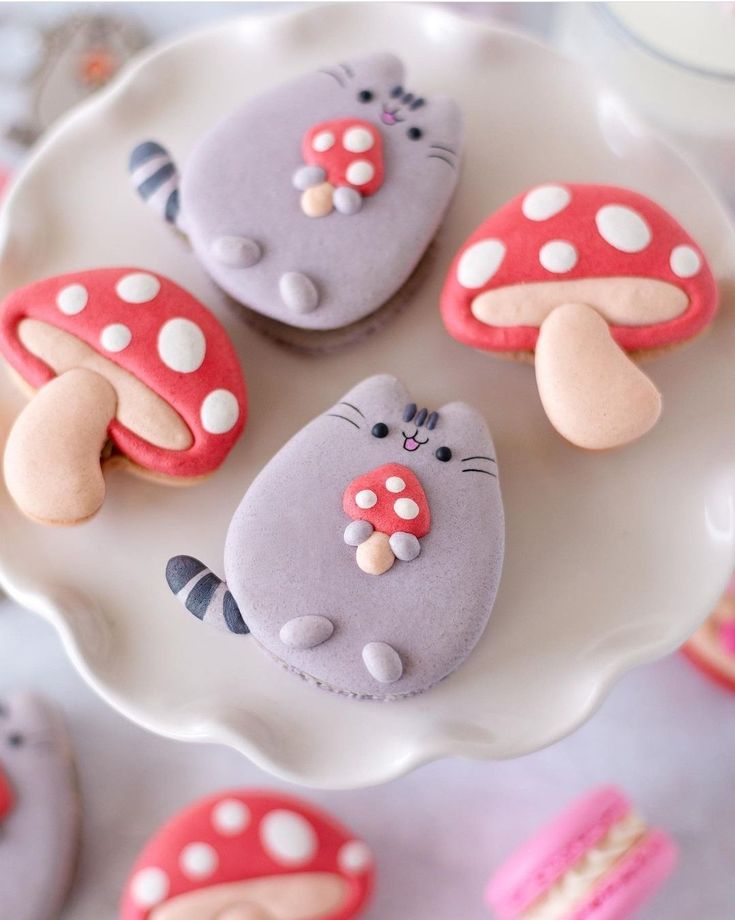 three decorated cookies sitting on top of a white plate next to pink and gray cupcakes