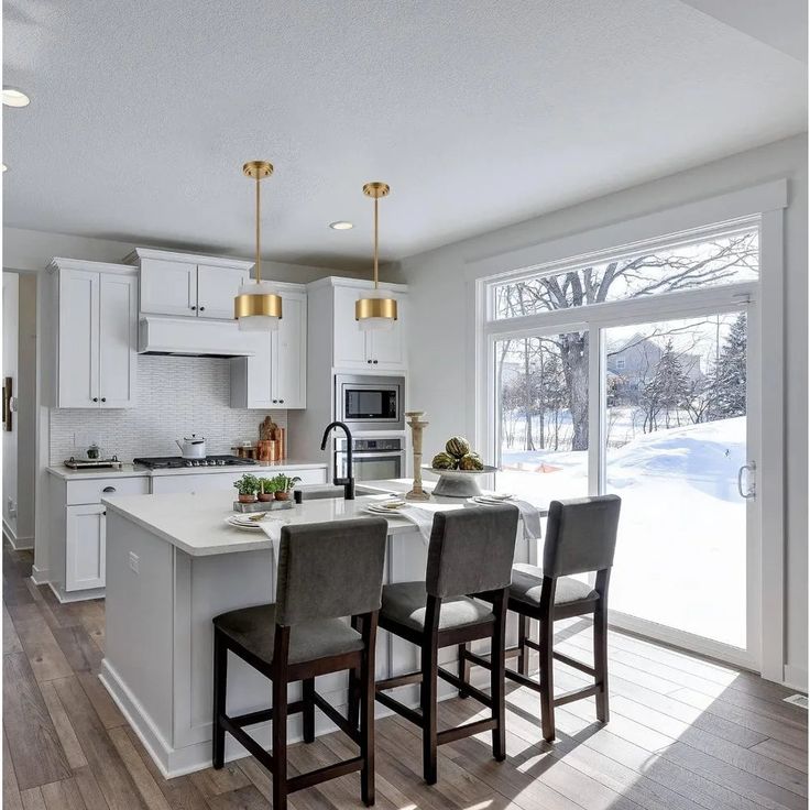 a kitchen with white cabinets and an island in front of a window that looks out onto the snow covered yard