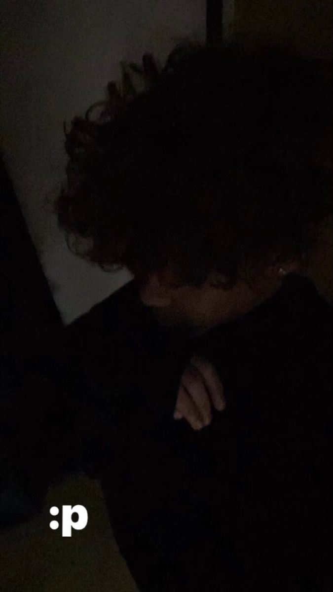 a woman with curly hair is looking down at her cell phone while sitting in the dark