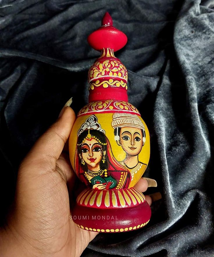 a hand holding a small decorative item in it's left hand, with an image of two people painted on the top