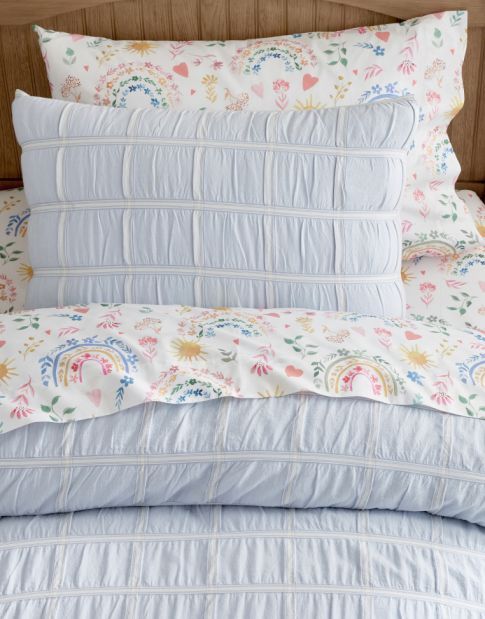 a bed with white and blue comforters on top of it next to a wooden headboard