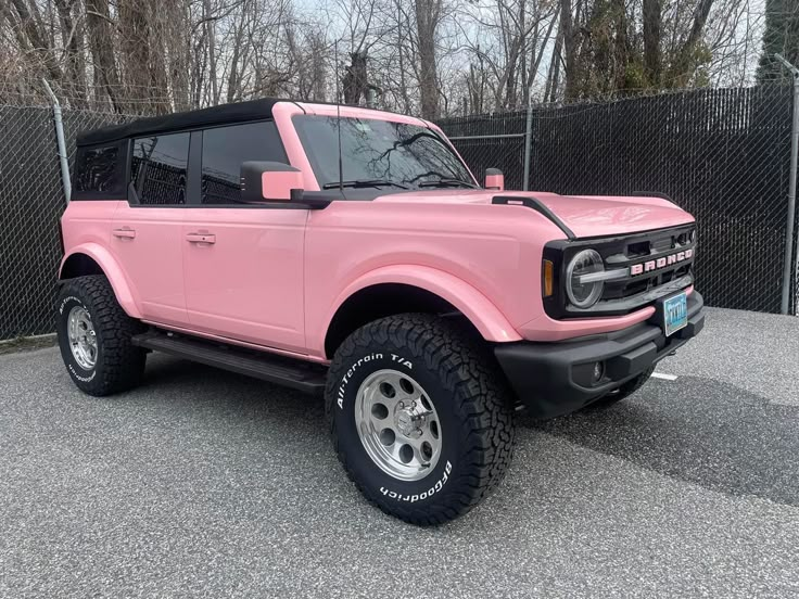 a pink pick up truck parked in a parking lot next to a chain link fence