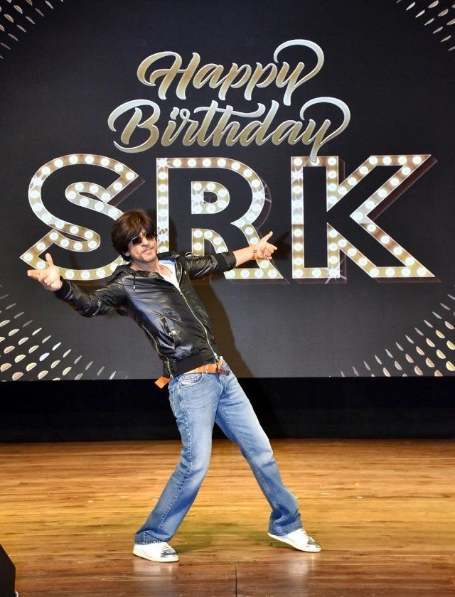 a man standing on top of a wooden floor in front of a sign that says happy birthday srk