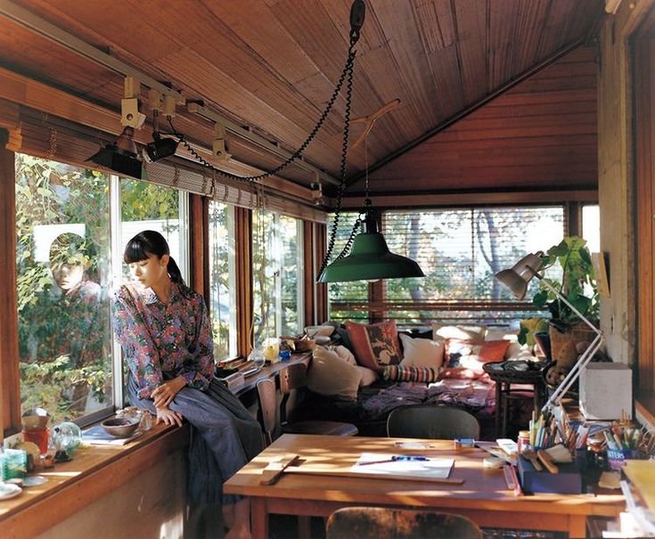 a woman sitting on a window sill next to a table and chair in a living room