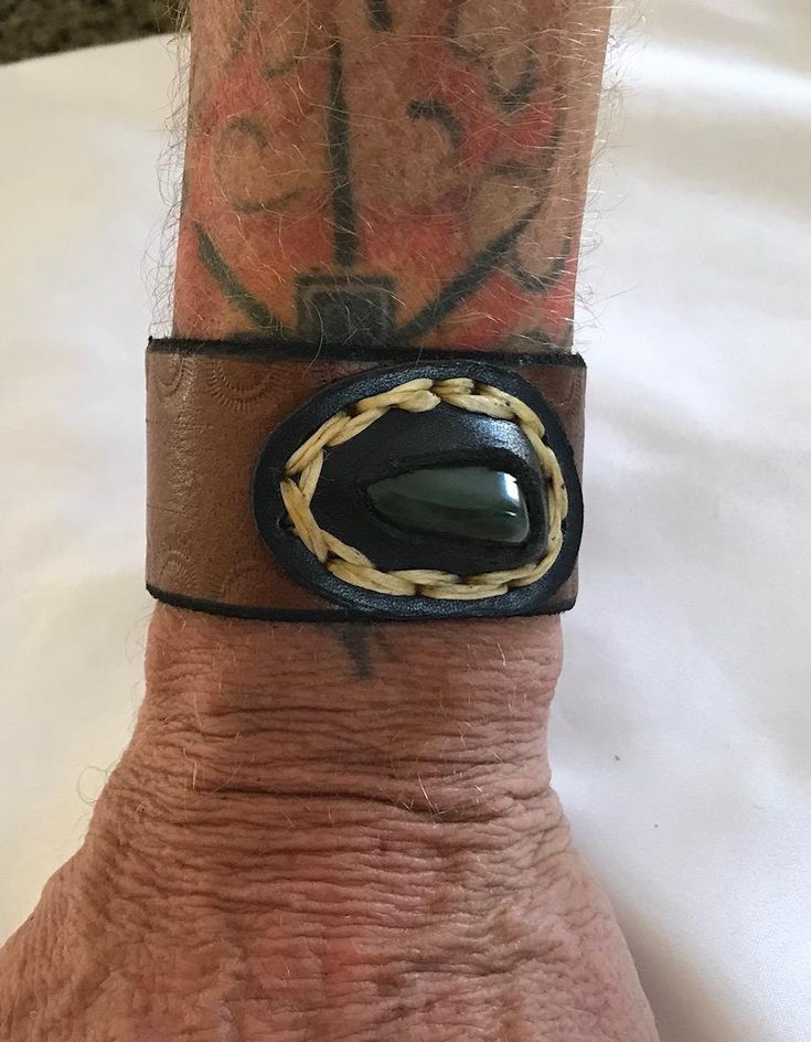 This is a unique handcrafted brown leather cuff with a good size jade nugget in a nice bezel setting (waxed threat) . The edges of the leather cuff are tooled, edged and stained..the cuff has 2 snaps for adjustment....the length of the wristband is 9 inches and fits a 7 or 6 inch wrist...the width is 1 1/2 inches the leather is a nice thick brown latigo and the snaps are copper. Artisan Adjustable Cuff Leather Bracelet, Brown Leather Cuff Jewelry, Leather Concho Cuff Bracelet, Leather Cuff Bracelet With Concho, Handmade Western Brown Cuff Bracelet, Handmade Western Style Brown Cuff Bracelet, Brown Leather Concho Bracelet, Unique Leather Cuff Jewelry, Adjustable Hand Wrapped Brown Cuff Bracelet