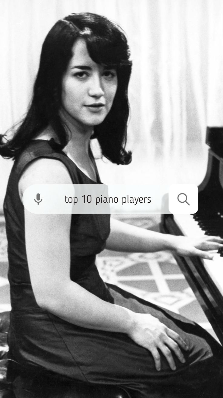 a woman sitting at a piano with her hands on the keyboard and looking into the camera