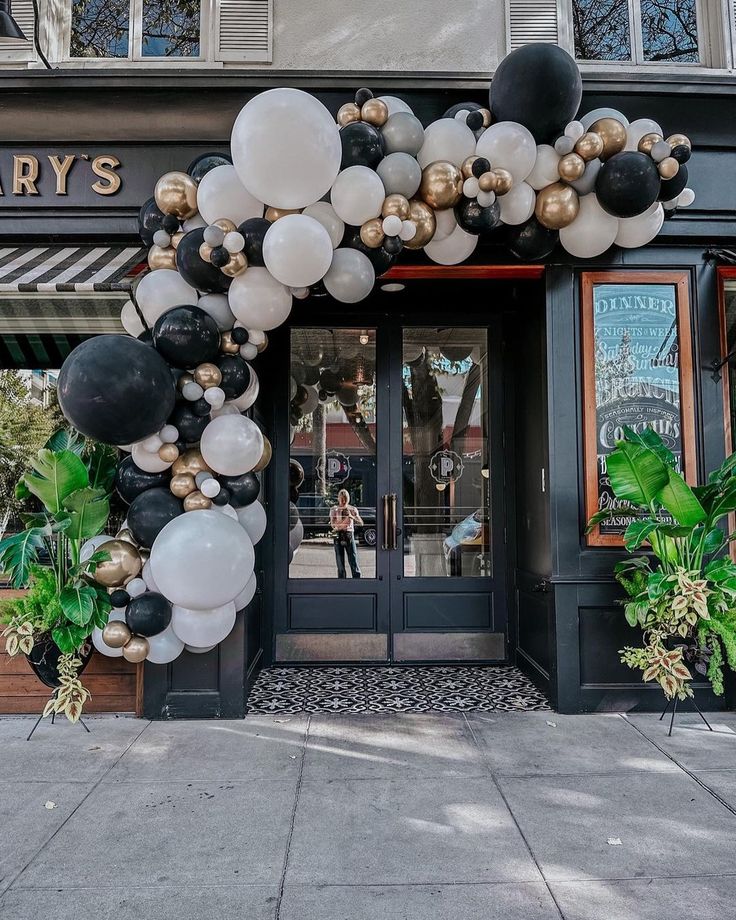 a large balloon arch in front of a store with black, white and gold balloons