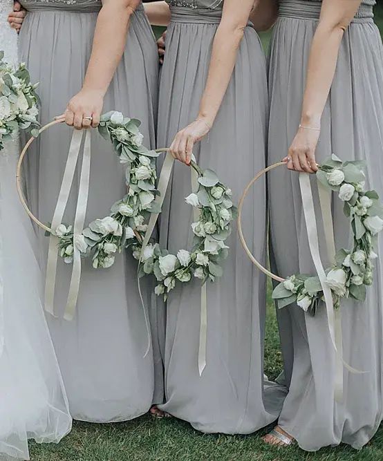 four bridesmaids holding wreaths with flowers and ribbons on them, all wearing gray dresses