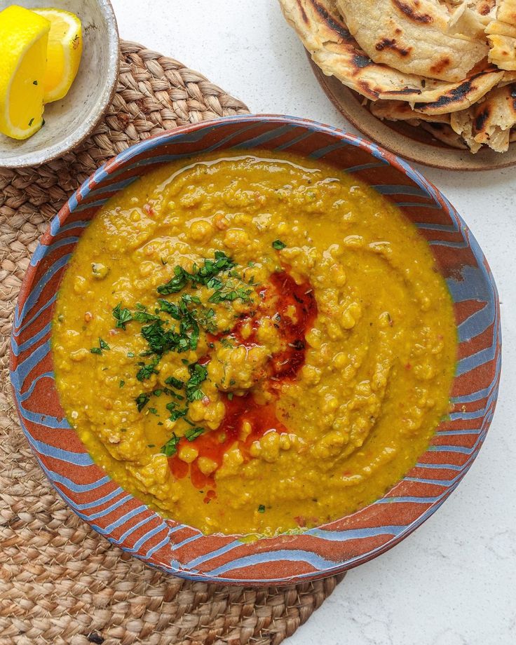 a bowl filled with yellow soup next to pita bread