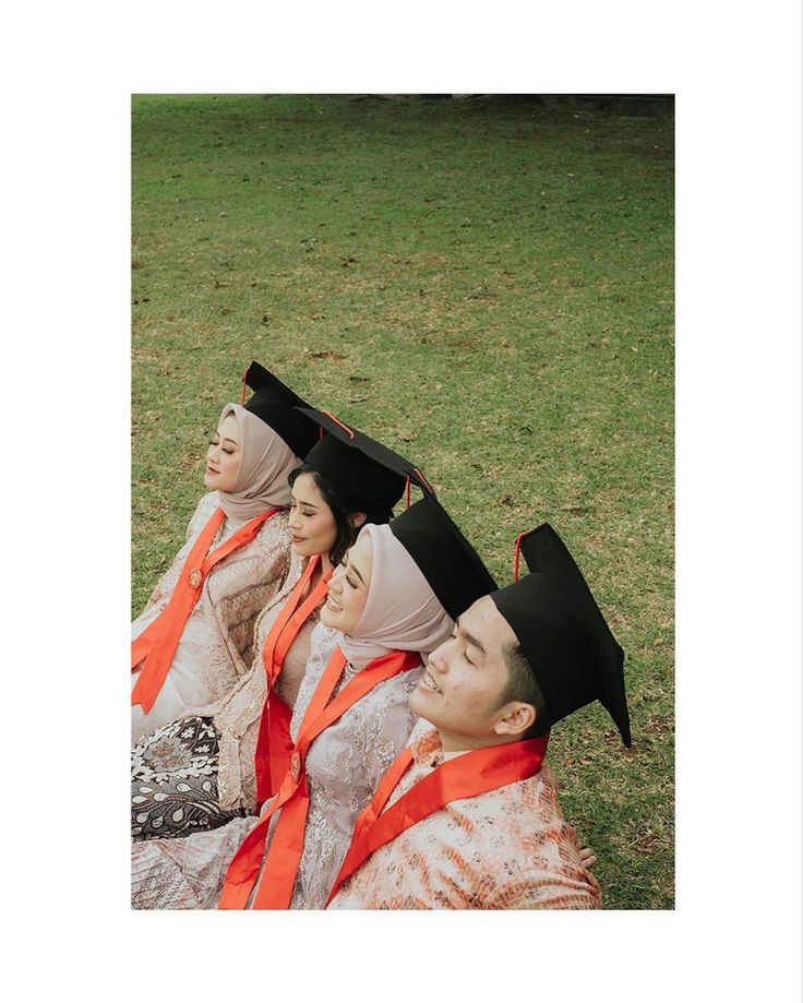 four people wearing headscarves sitting on the ground in front of a grassy field