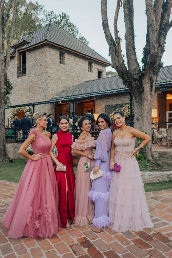 four women in long dresses posing for the camera on a brick walkway with trees behind them