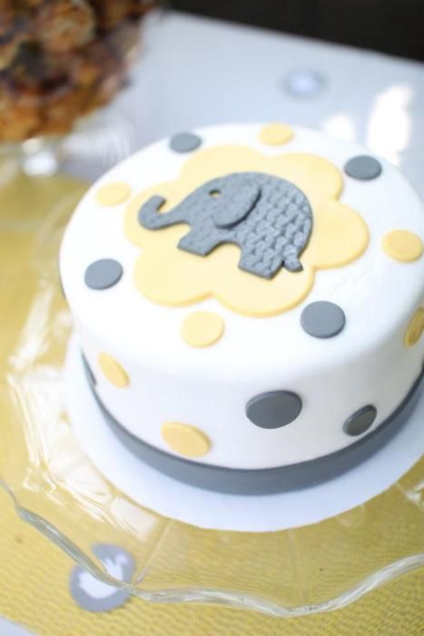 a white cake with grey and yellow polka dots on the bottom is decorated with an elephant