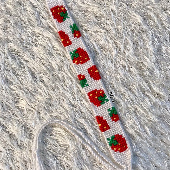 an apple themed bracelet with red apples and green leaves on white furnishing next to a pair of scissors