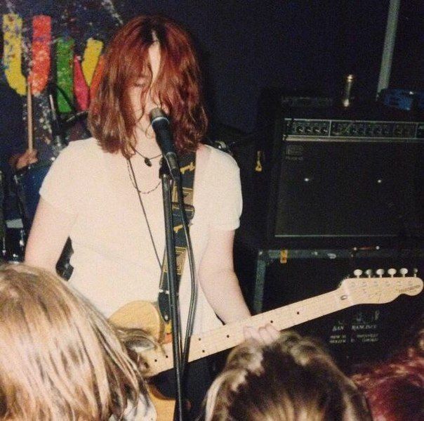 a man with long hair playing guitar in front of a group of people at a concert